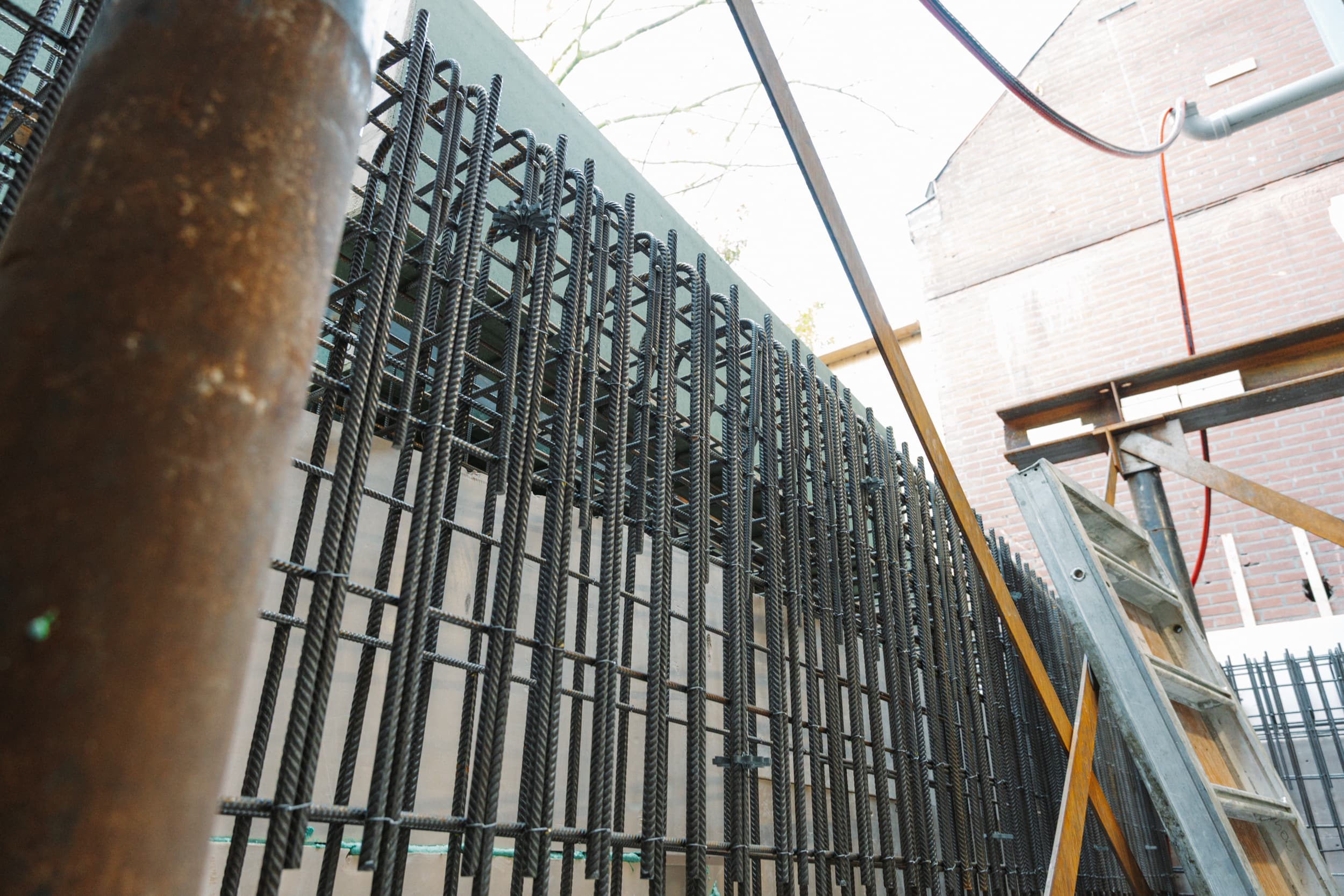 Wapening voor een betonnen wand tijdens werkzaamheden van Bouwcon naast een bestaande woning